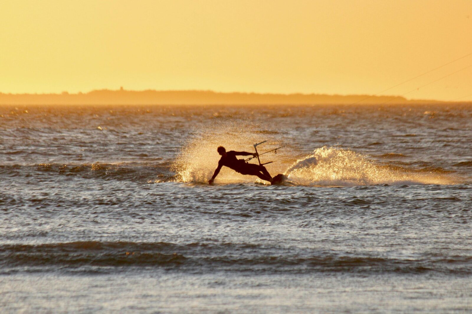 Kite surfer creating splashes against sunset backdrop. Vivid silhouette on open water.